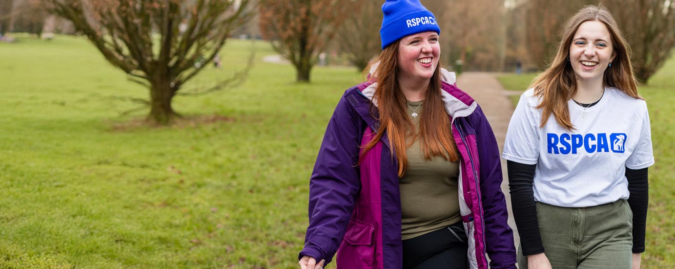 Two RSPCA fundraisers taking part in a walking event. The person to the left wearing a blue RSPCA branded beanie, and the person to the right wearing a white branded t-shirt with a blue RSPCA logo.