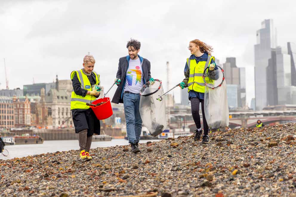 Three volunteer litter pickers on the banks of the river Thames in London.