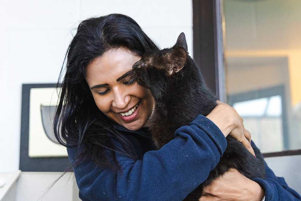 Smiling lady cuddling a black cat.